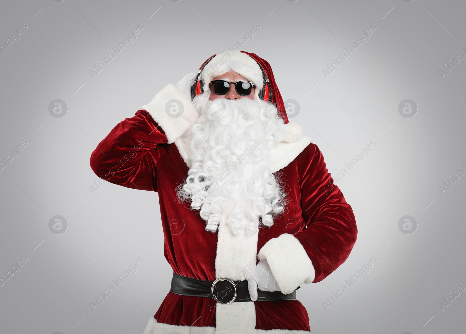 Photo of Santa Claus with headphones listening to Christmas music on light grey background