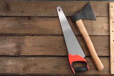 Photo of Saw with colorful handle and axe on wooden background, flat lay. Space for text