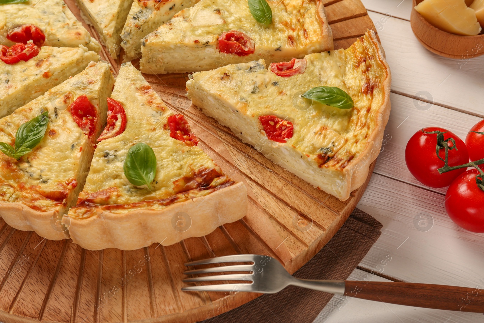 Photo of Delicious homemade cheese quiche, fork and ingredients on white wooden table, closeup