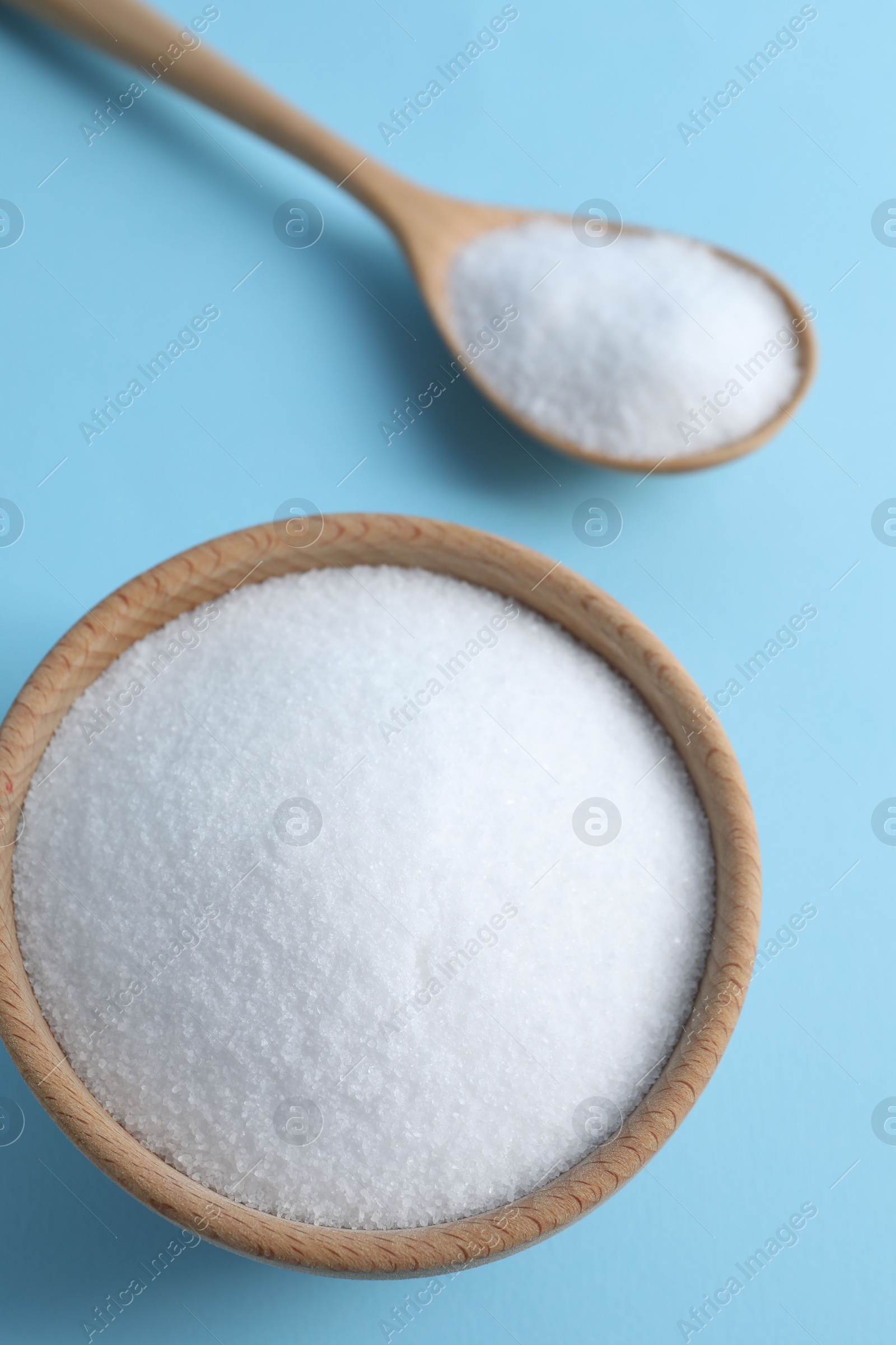 Photo of Organic white salt in bowl and spoon on light blue background, above view