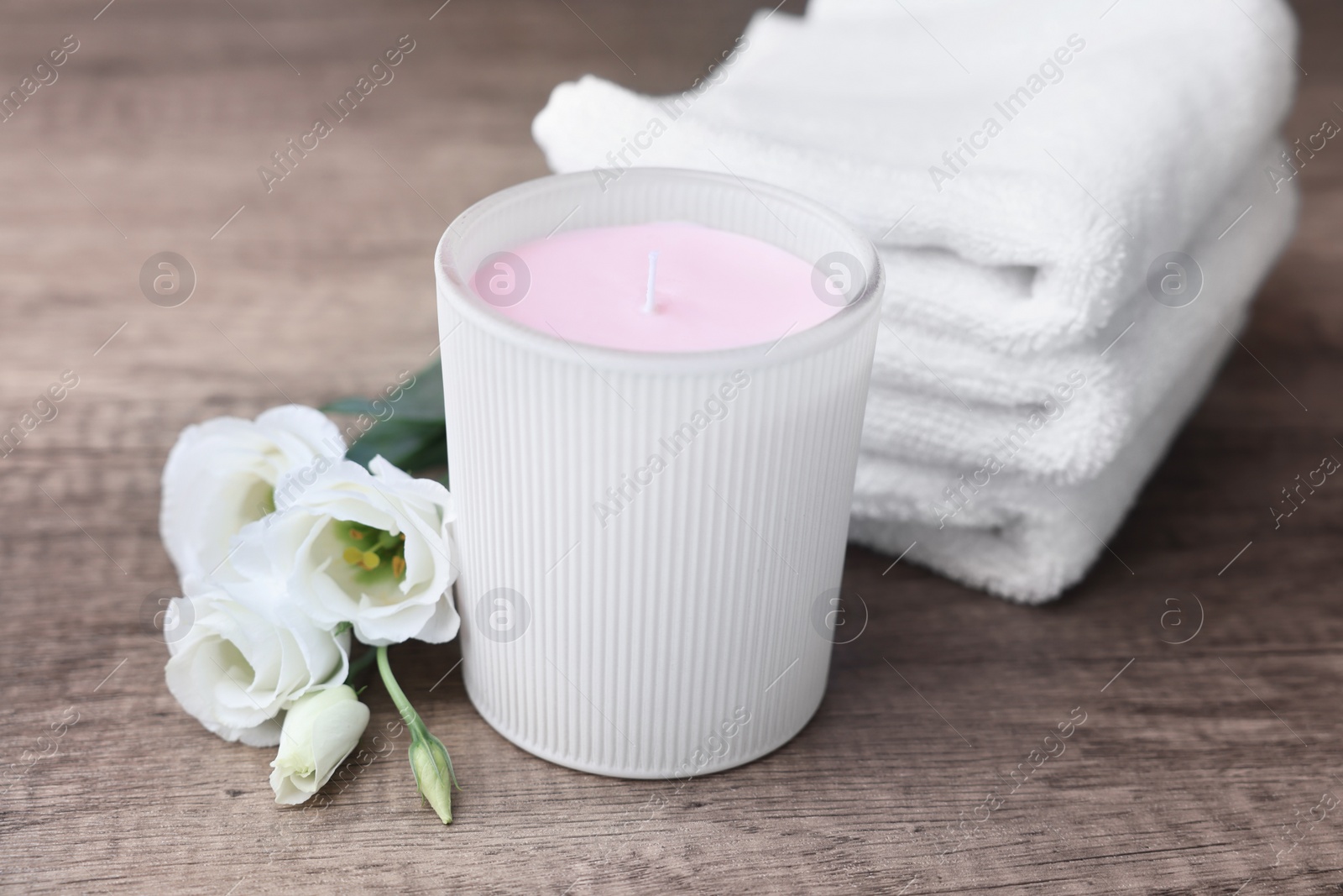 Photo of Scented candle, folded towels and eustoma flowers on wooden table