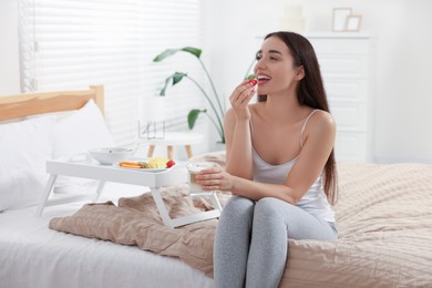 Photo of Happy young woman having breakfast near white tray on bed at home