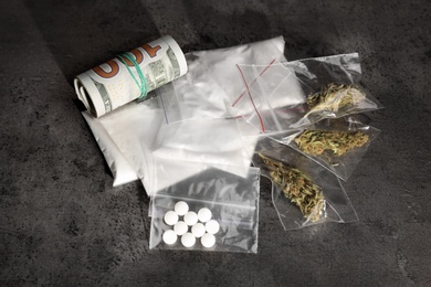 Photo of Plastic bags with cocaine, pills, hemp buds and money on grey background
