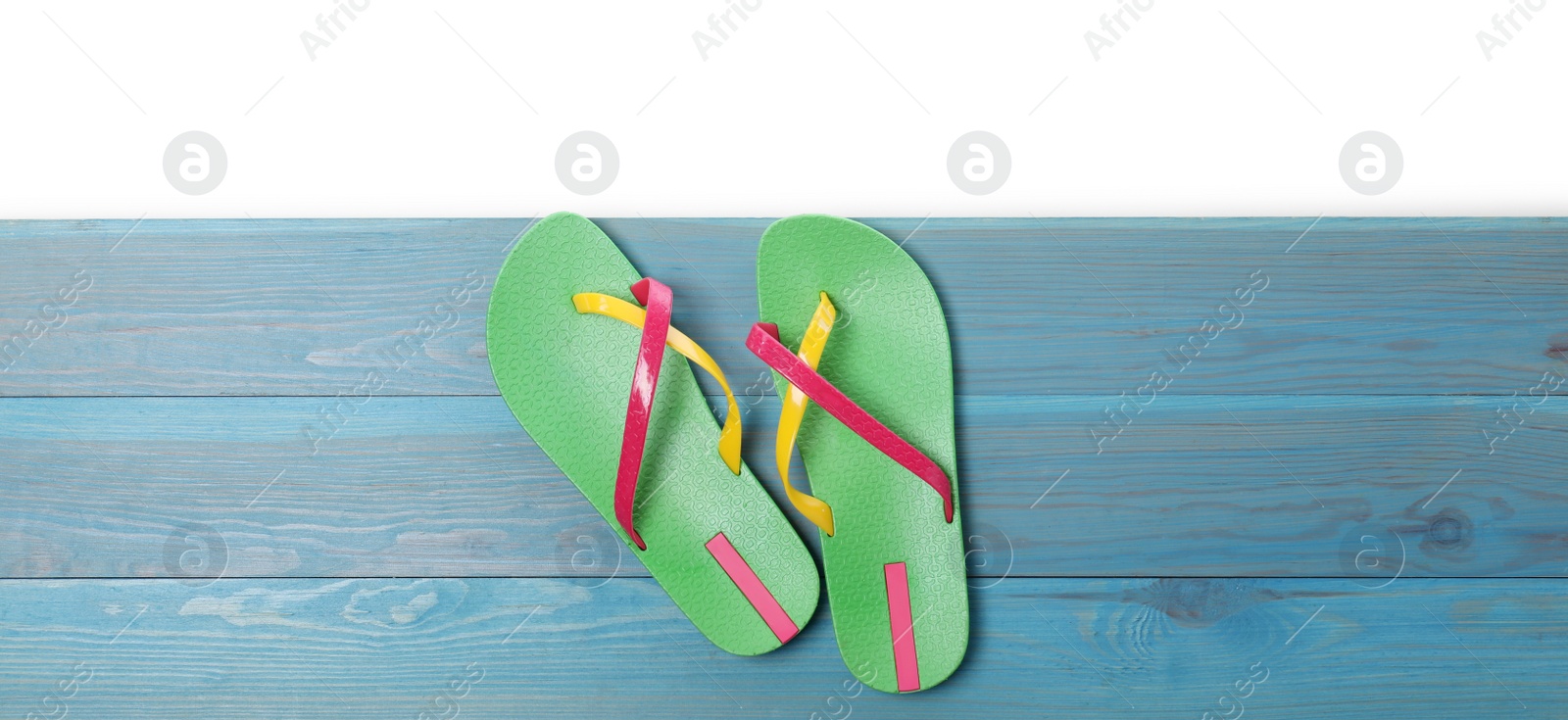 Photo of Green flip flops on turquoise wooden table against white background, top view