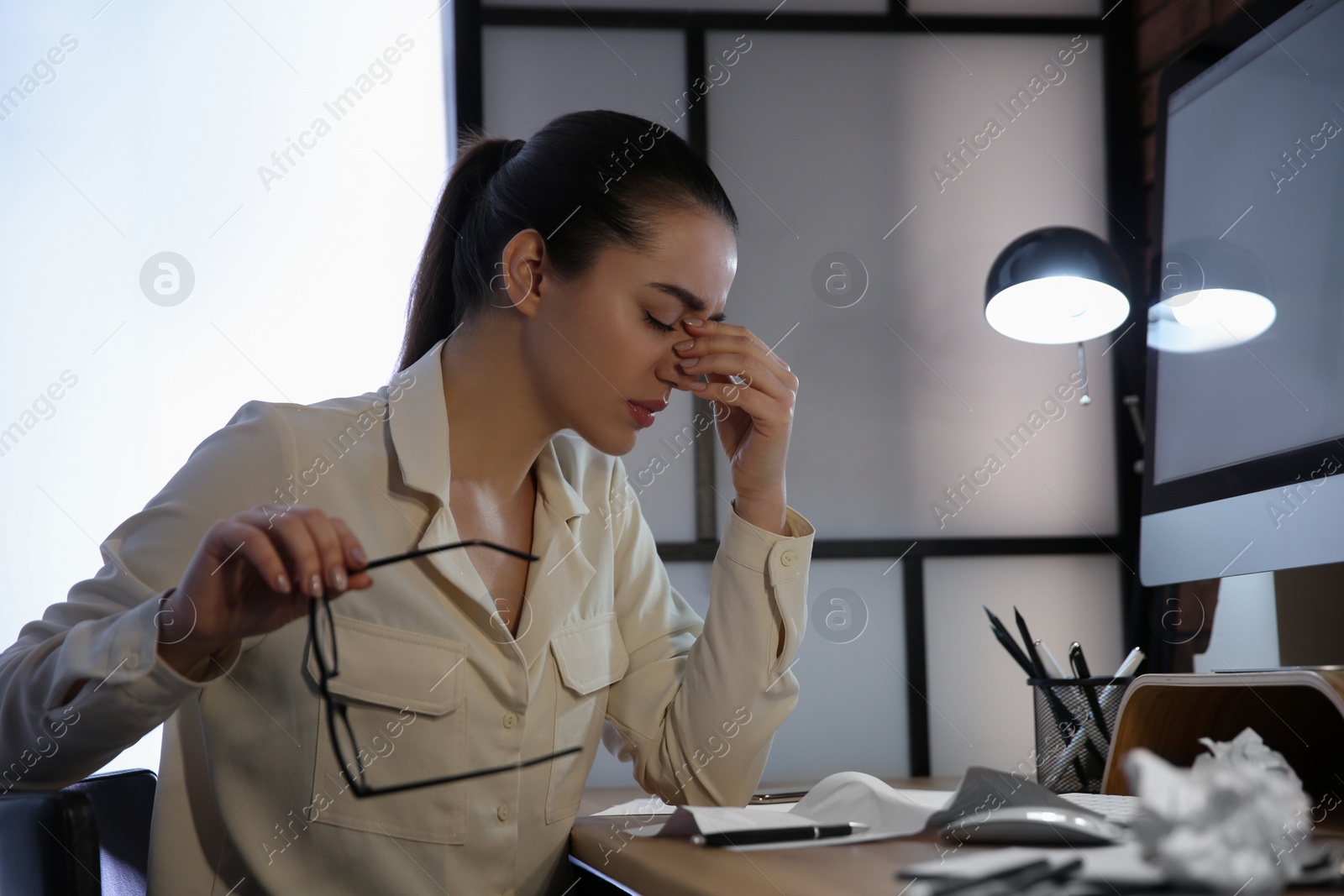 Photo of Stressed and tired young woman with headache at workplace