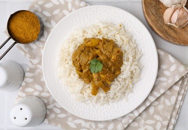 Photo of Delicious chicken curry with rice and ingredients on white tiled table, flat lay