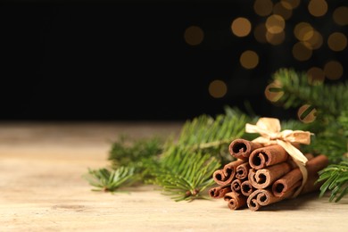 Photo of Bunch of cinnamon sticks and fir branches on wooden table against black background. Space for text