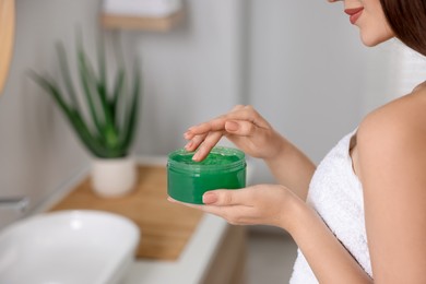 Photo of Young woman holding jar of aloe hair mask indoors, closeup. Space for text