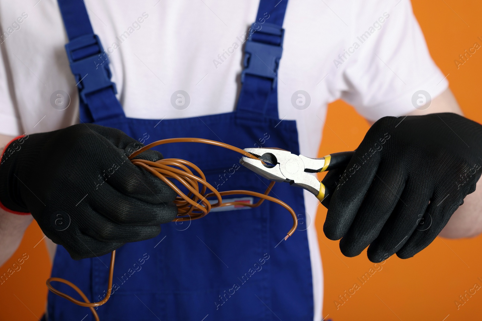 Photo of Young man holding pliers and wires on orange background, closeup