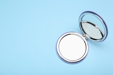 Stylish cosmetic pocket mirror on light blue background, top view. Space for text