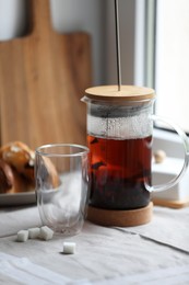 Photo of Teapot with freshly brewed tea, empty glass and sugar cubes on table near window