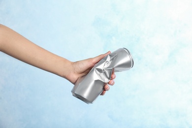 Photo of Woman holding crumpled aluminum can on color background. Metal waste recycling