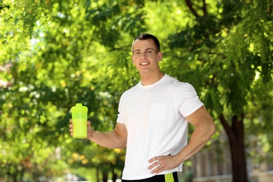 Athletic young man with protein shake at green park