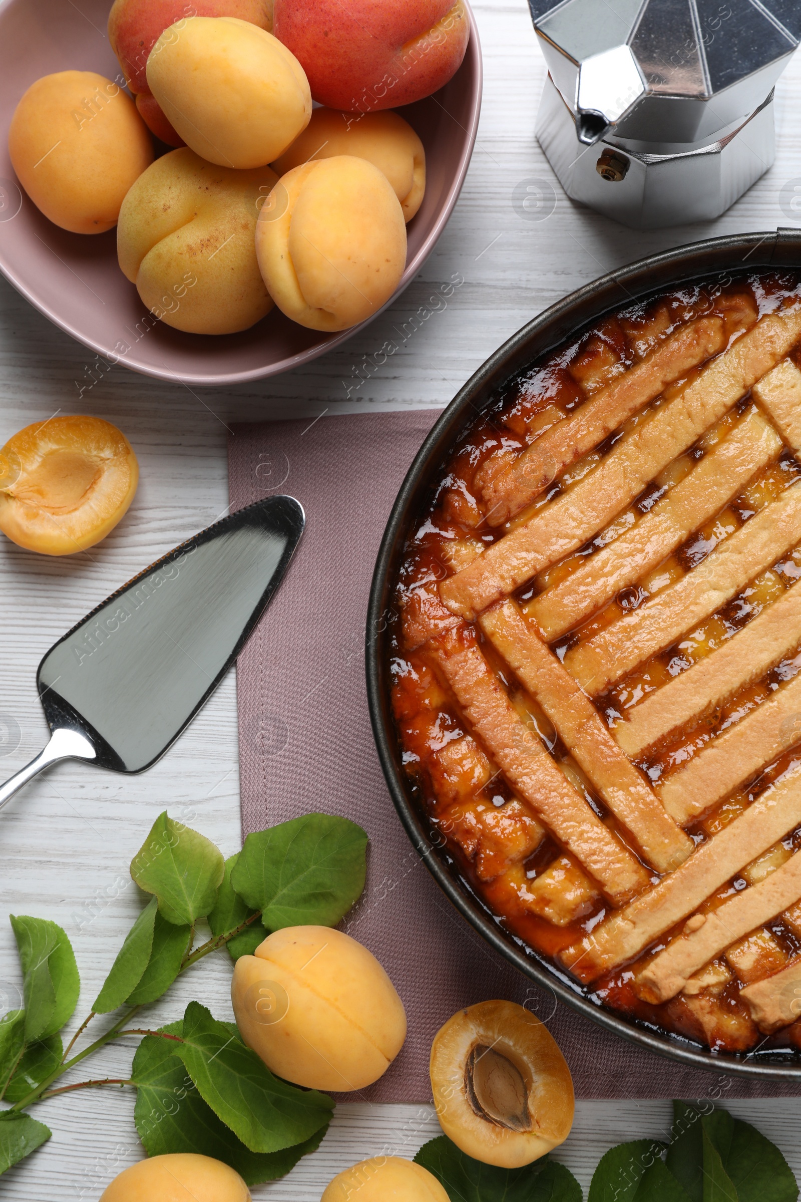 Photo of Delicious apricot pie in baking dish and fresh fruits on white wooden table, flat lay