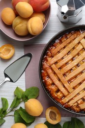 Delicious apricot pie in baking dish and fresh fruits on white wooden table, flat lay