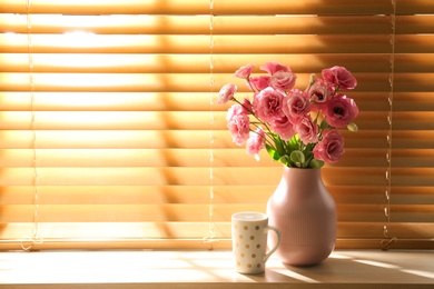 Photo of Vase with flowers and cup on wooden window sill in room, space for text