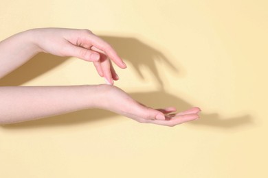 Woman applying cream on her hand against yellow background, closeup