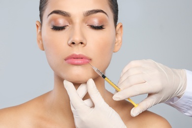 Young woman getting lips injection on grey background. Cosmetic surgery