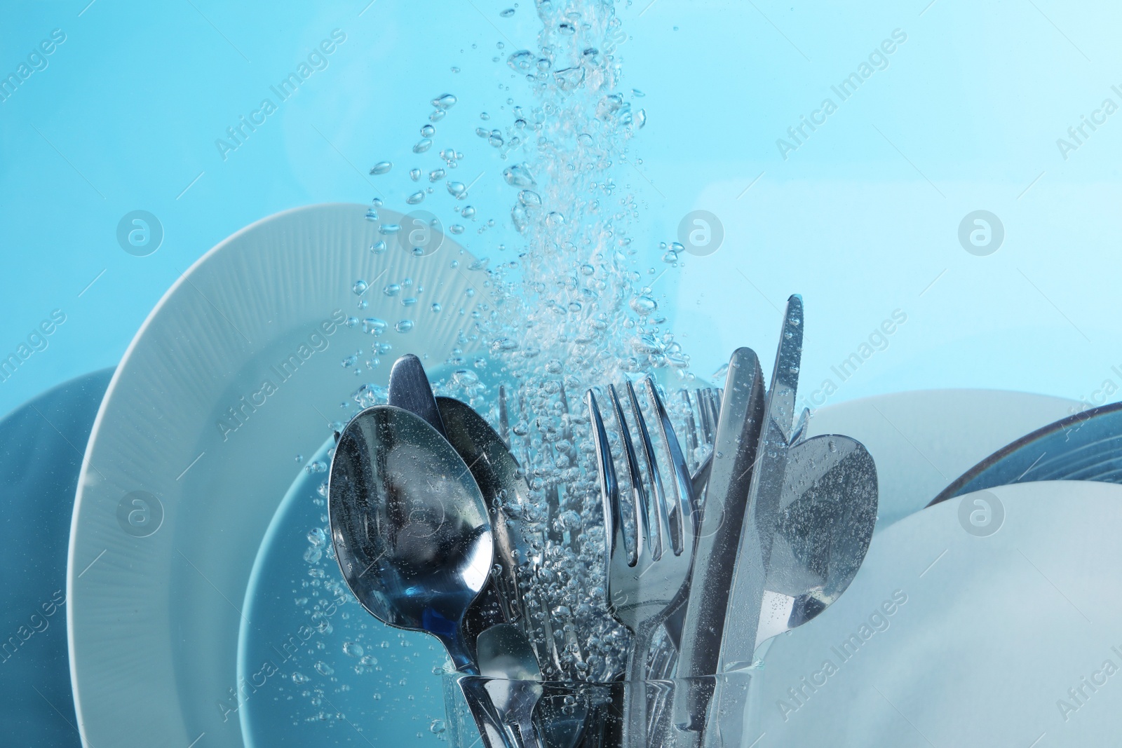 Photo of Washing silver cutlery and plates in water on light blue background