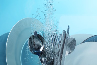 Washing silver cutlery and plates in water on light blue background