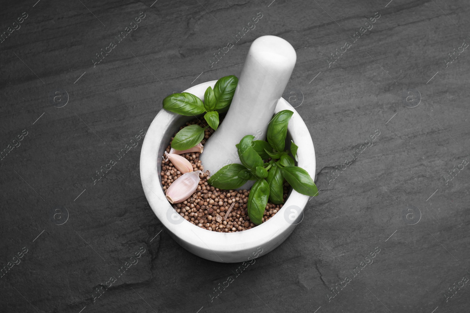 Photo of Mortar with peppercorns, basil and garlic on black table, above view