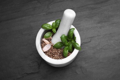 Mortar with peppercorns, basil and garlic on black table, above view