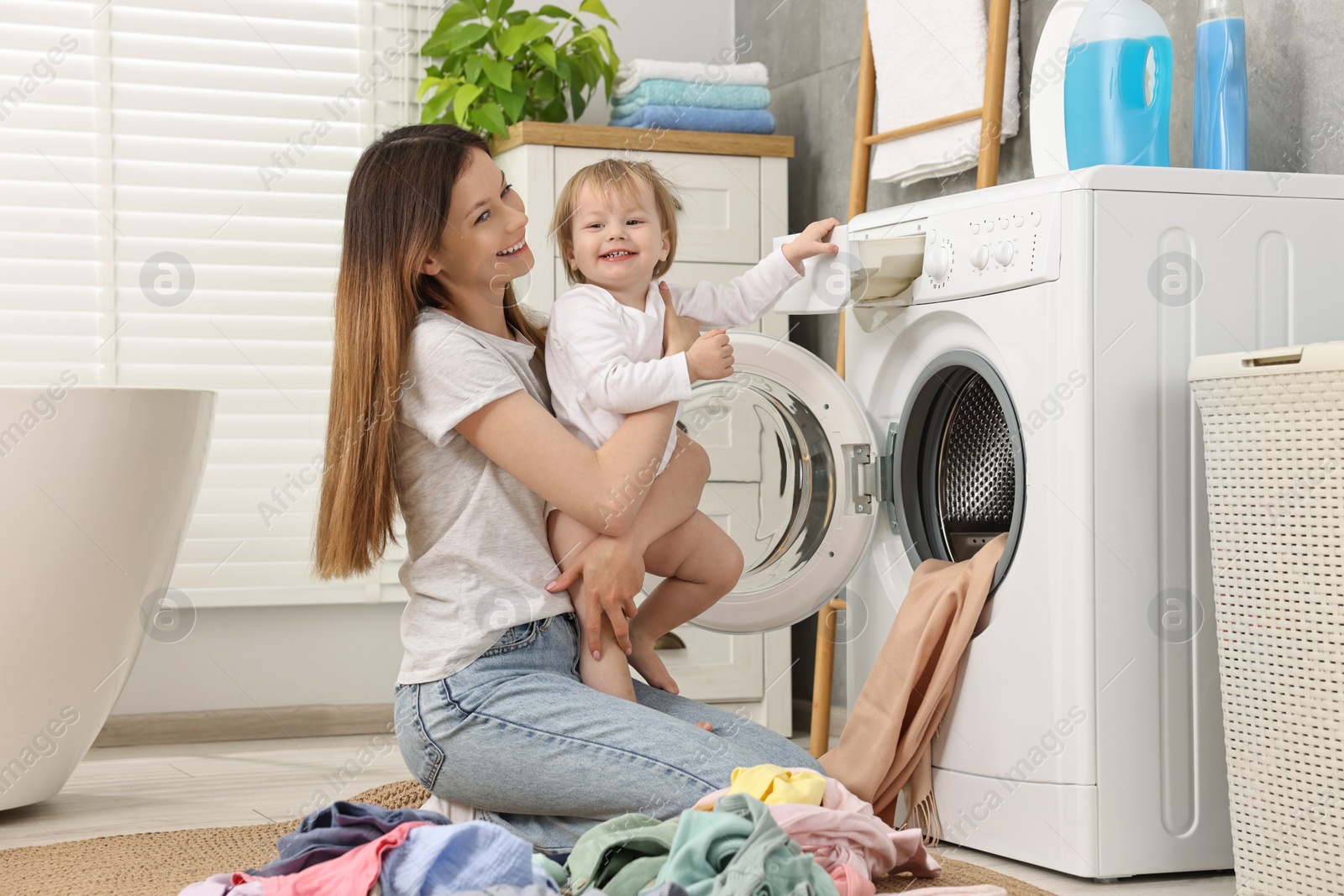 Photo of Happy mother with her daughter having fun while washing baby clothes in bathroom