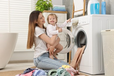 Happy mother with her daughter having fun while washing baby clothes in bathroom