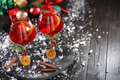 Photo of Christmas Sangria cocktail in glasses and snow on dark wooden table, space for text