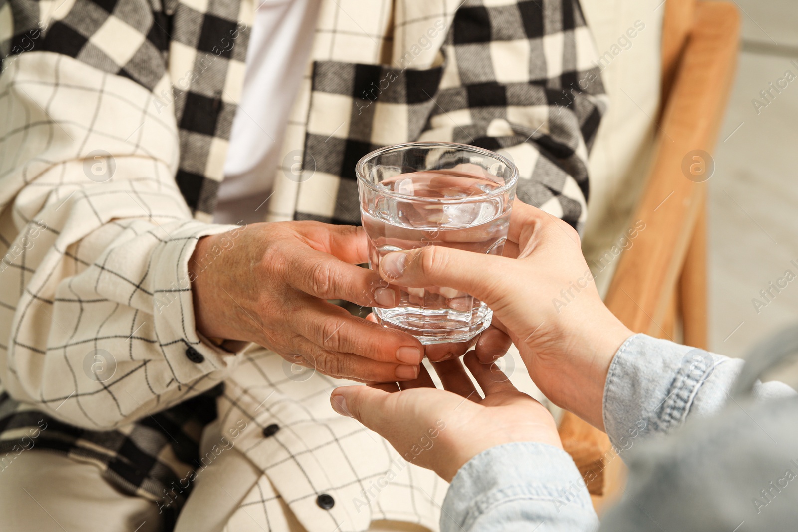 Photo of Caretaker giving glass of water to elderly woman indoors, closeup