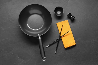 Empty iron wok, sauce bowl and chopsticks on black table, flat lay