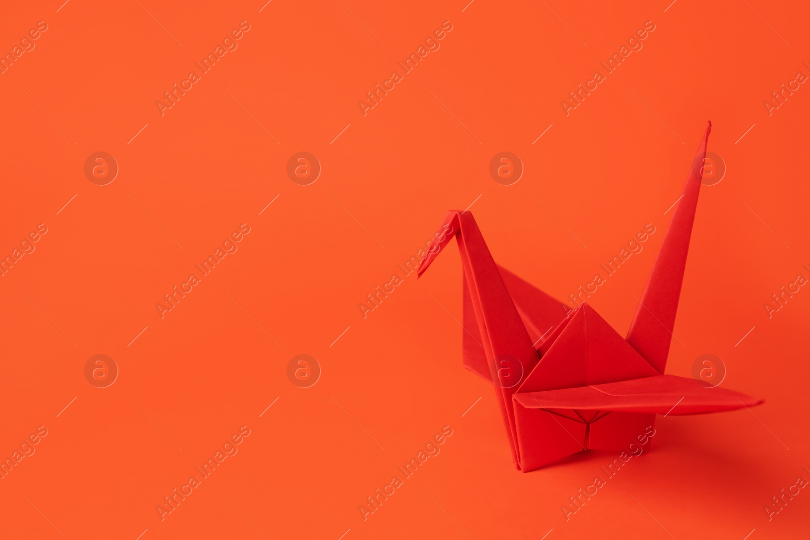 Photo of Origami art. Handmade paper crane on orange background, space for text