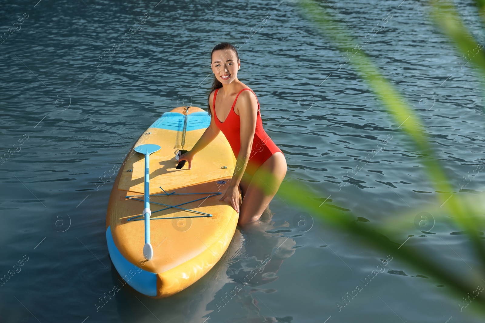 Photo of Young woman standing near SUP board in river water on sunny day