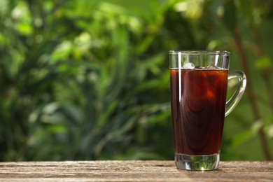 Photo of Glass of iced coffee on wooden table outdoors. Space for text