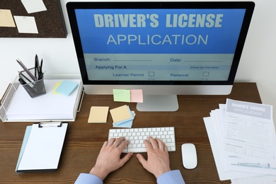 Man using computer to fill driver's license application form at table in office, closeup