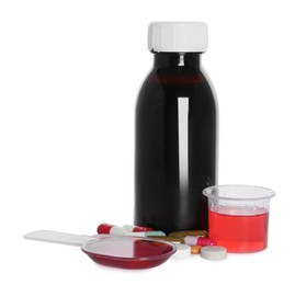 Bottle of cough syrup, dosing spoon, measuring cup and pills on white background