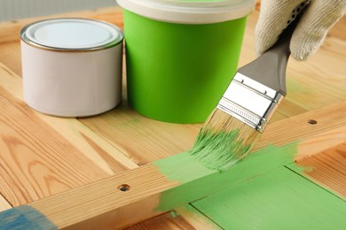 Photo of Worker applying green paint onto wooden surface, closeup