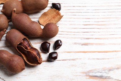 Photo of Delicious ripe tamarinds on white wooden table, above view. Space for text