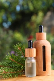 Photo of Bottles of pine essential oil and branches on wooden table against blurred background, closeup