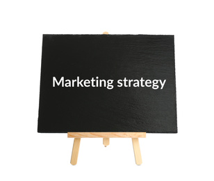 Blackboard with phrase MARKETING STRATEGY on wooden easel against white background