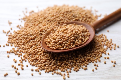 Photo of Mustard seeds with wooden spoon on white table, closeup