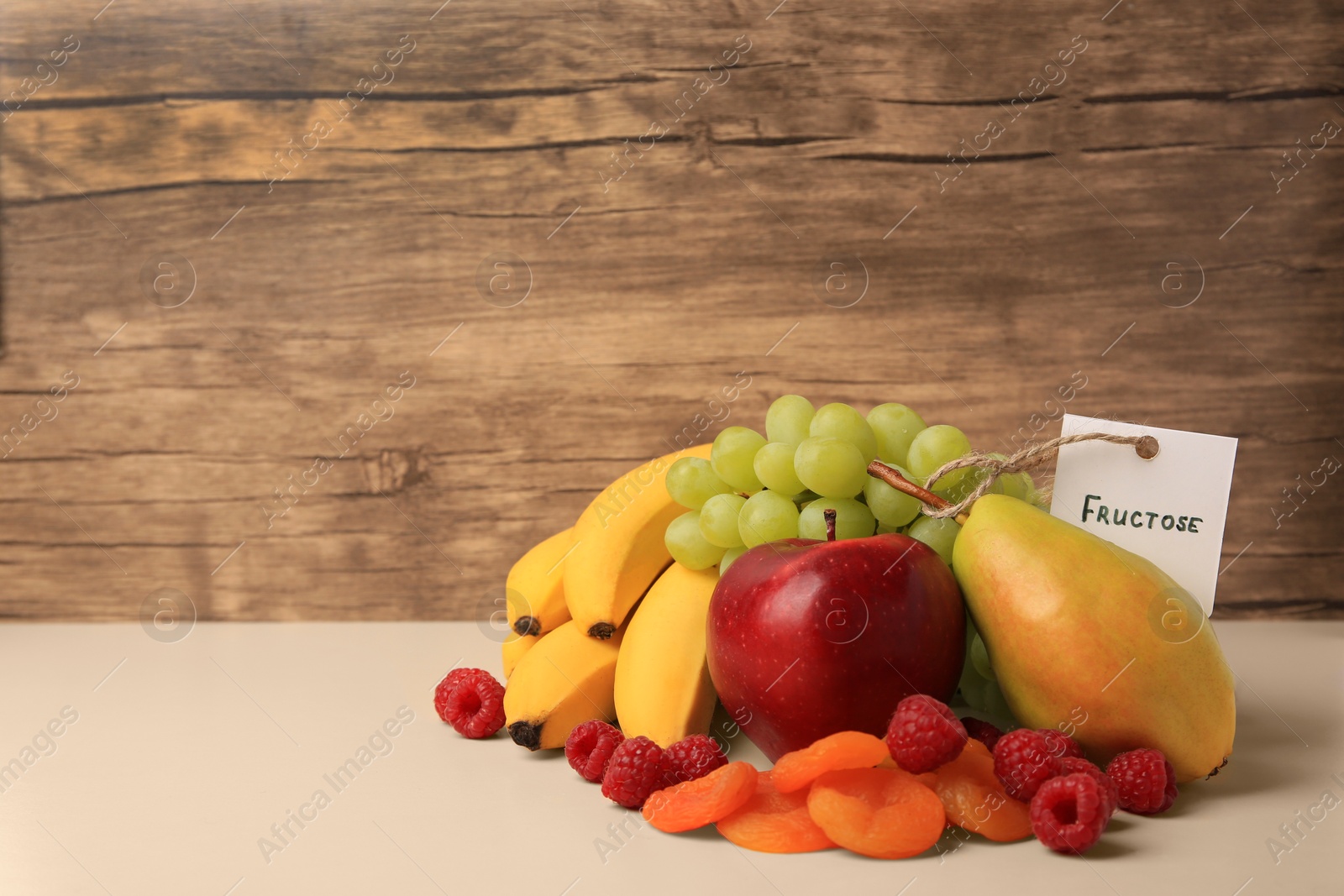 Photo of Card with word Fructose, delicious ripe fruits, raspberries and dried apricots on beige table, space for text