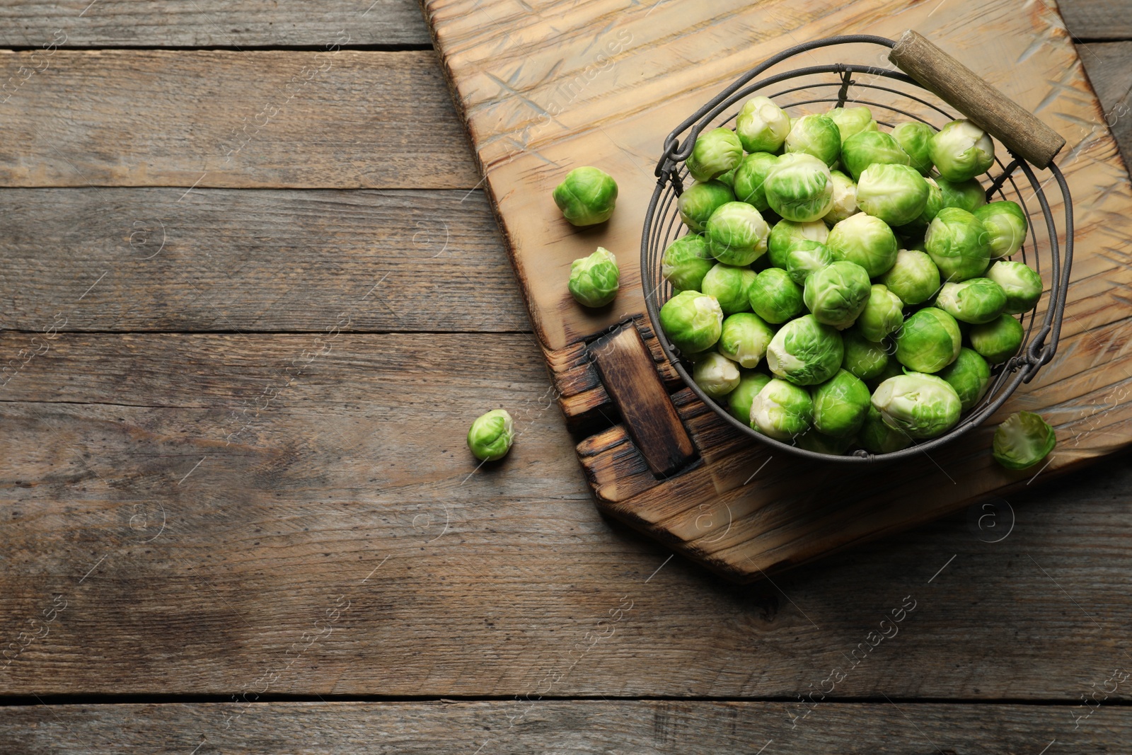 Photo of Metal basket with fresh Brussels sprouts on wooden background, top view. Space for text