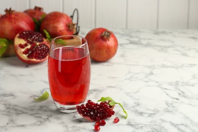 Photo of Tasty pomegranate juice in glass and fresh fruits on white marble table. Space for text