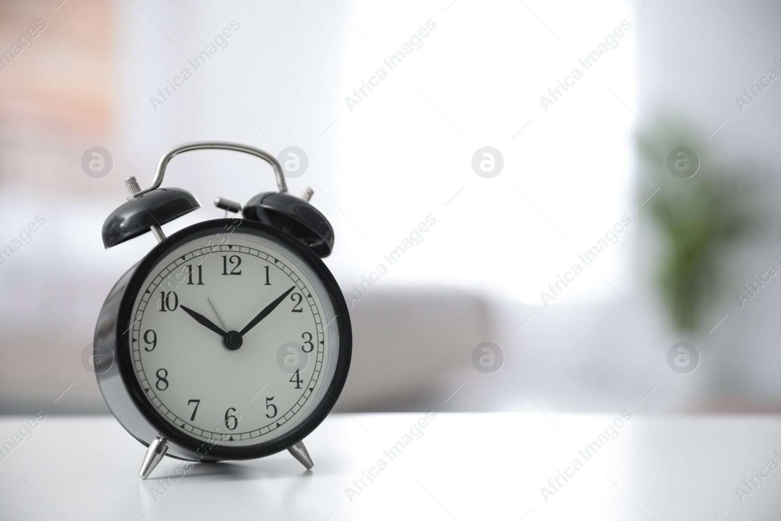 Photo of Black alarm clock on white table indoors. Space for text