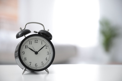 Black alarm clock on white table indoors. Space for text