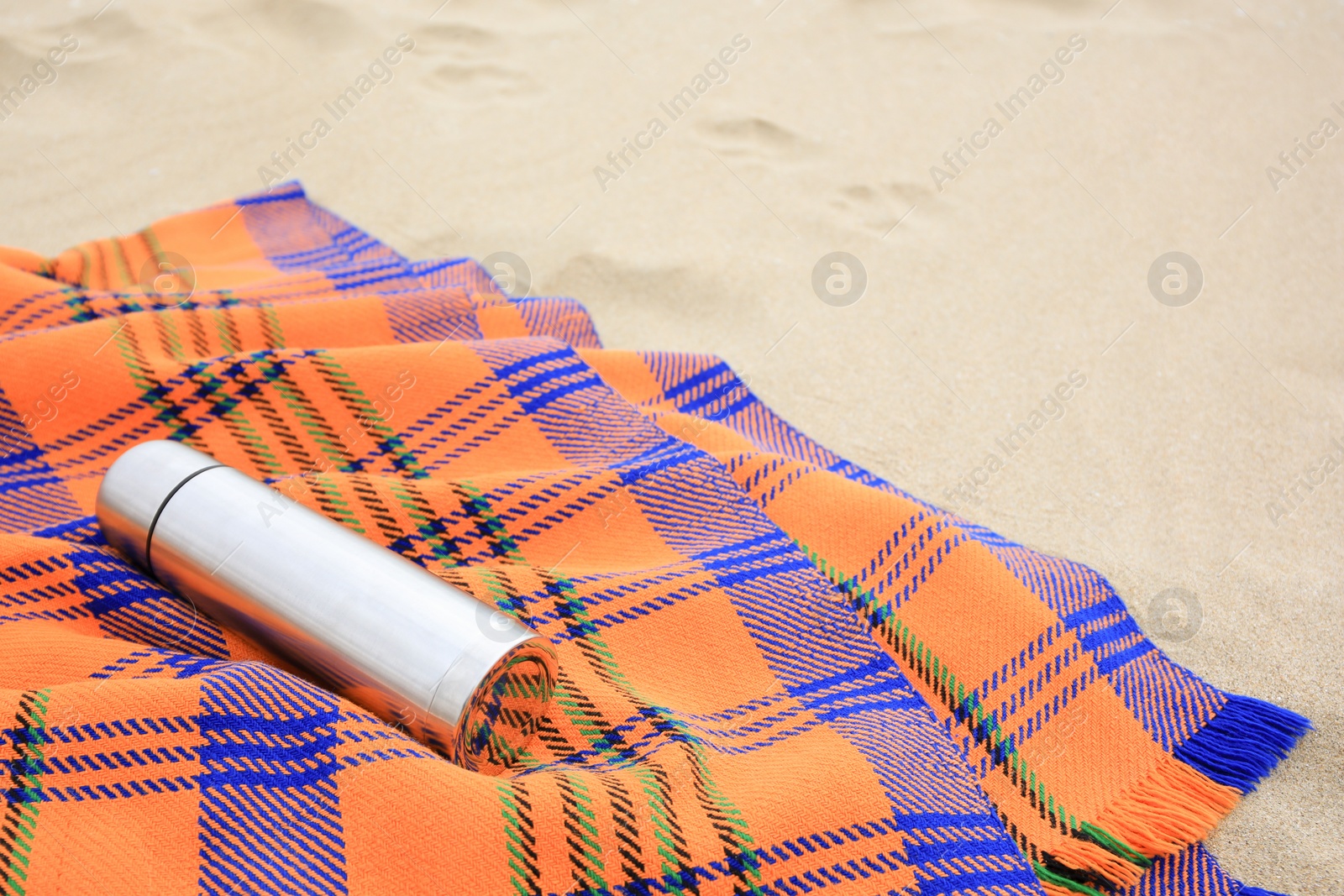 Photo of Metallic thermos with hot drink and plaid on sandy beach, space for text