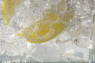 Juicy lemon slices and ice cubes in soda water against white background, closeup