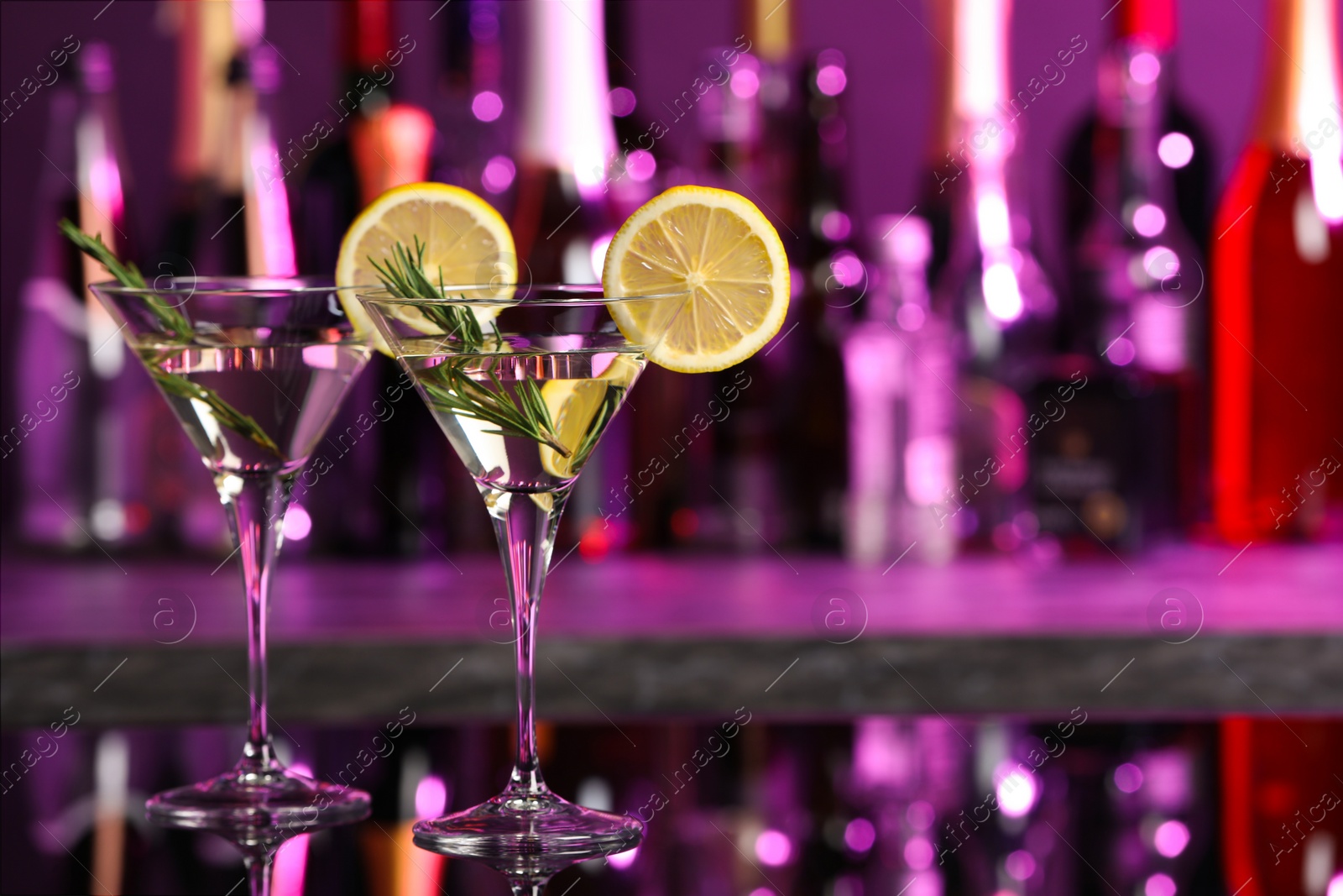 Photo of Martini glasses of refreshing cocktail, lemon slices and rosemary on mirror surface, space for text