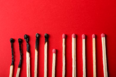 Burnt and whole matches on red background, flat lay. Stop destruction concept